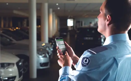 Security guard using the SequriX mobile patrol app in a car dealership.